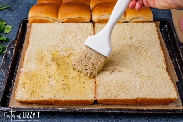 brushing butter over sliced rolls