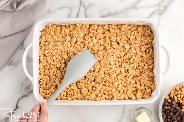 spatula pressing cereal bars in a baking pan