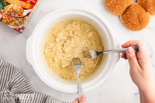 shredding chicken in a slow cooker with two forks