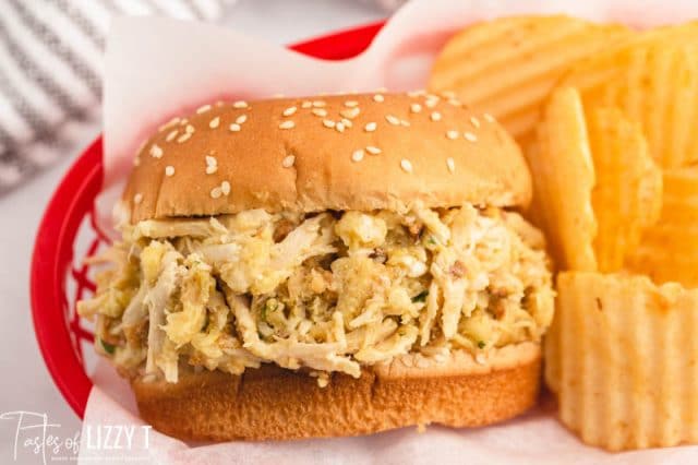 a shredded chicken sandwich in a basket with chips