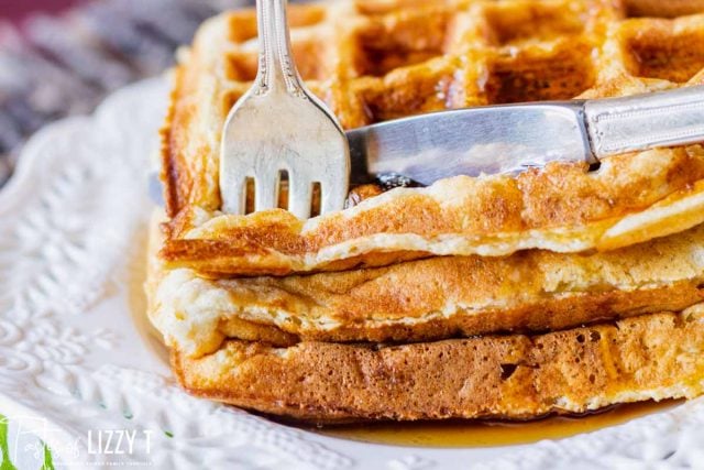 a knife and fork cutting into a stack of waffles