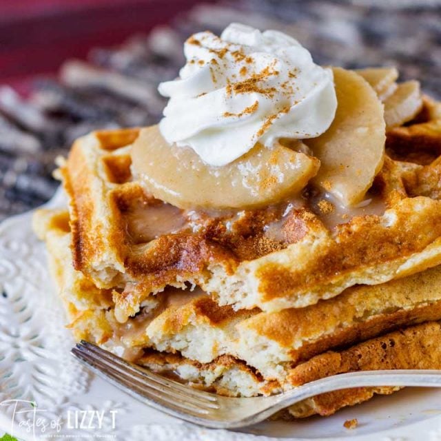 three waffles sitting on a plate with apples and whipped cream