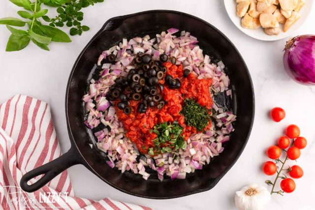 onions in a skillet with fresh herbs, tomatoes and olives