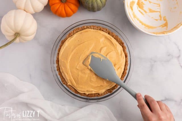 spreading pumpkin cheesecake filling into pie crust