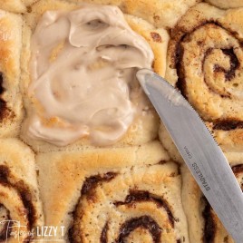 spreading cinnamon roll icing on a sweet roll
