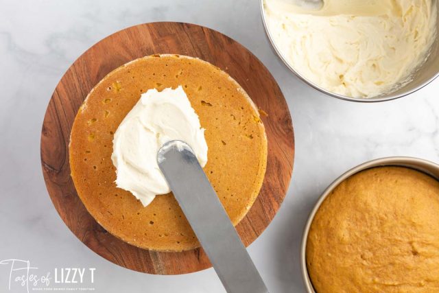 spreading cream cheese frosting on a cake