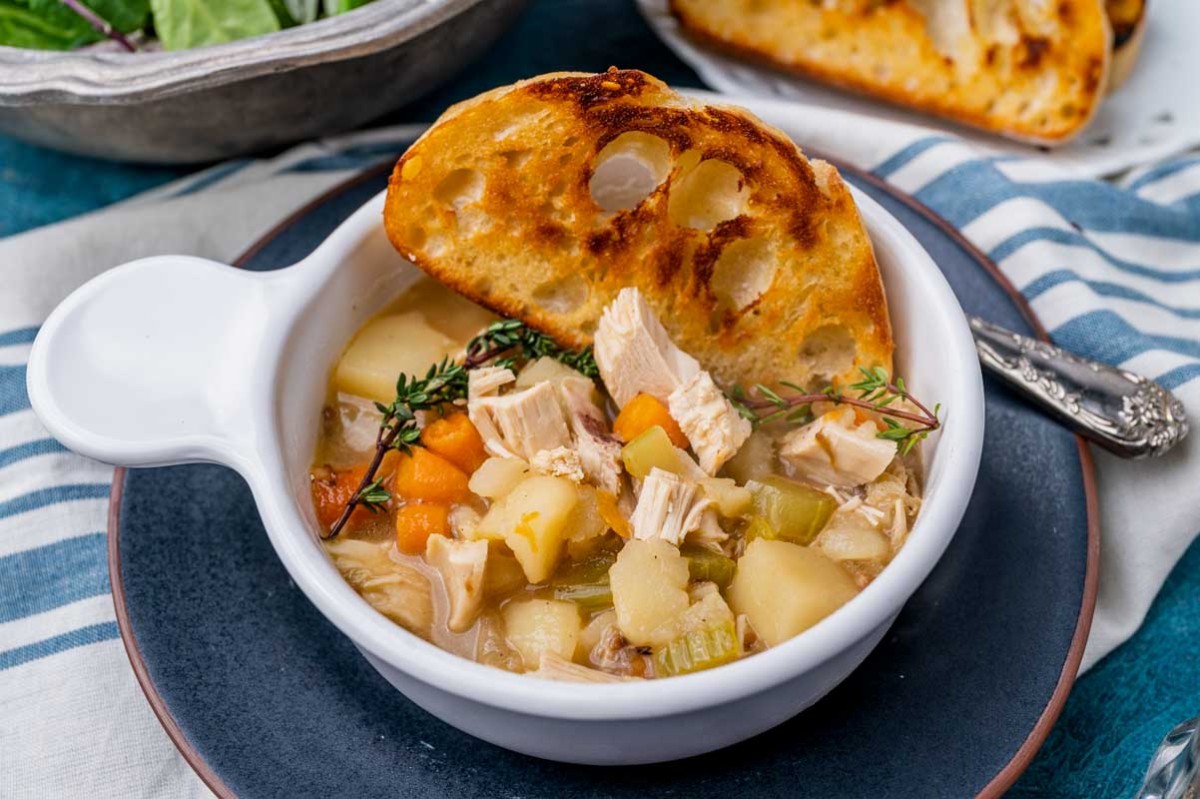 a bowl of potato chicken soup with a piece of buttered bread