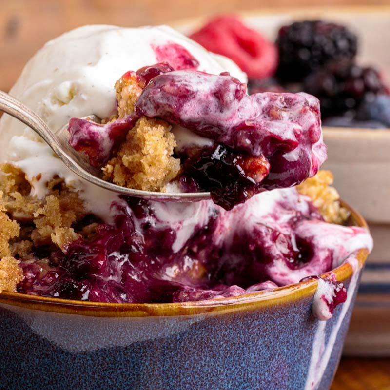 mixed berry crisp in a bowl with ice cream