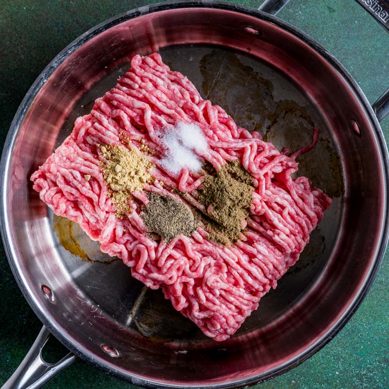 overhead view of ground pork and seasoning in a skillet