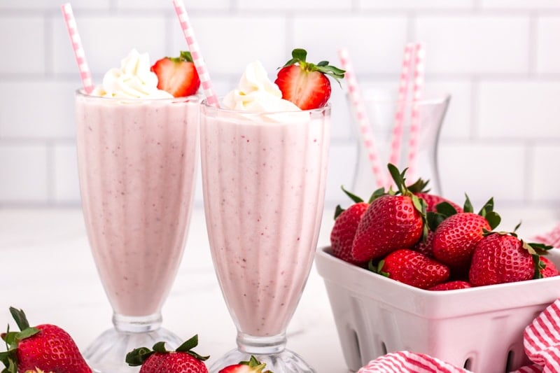 two strawberry milkshakes with straws & whipped cream