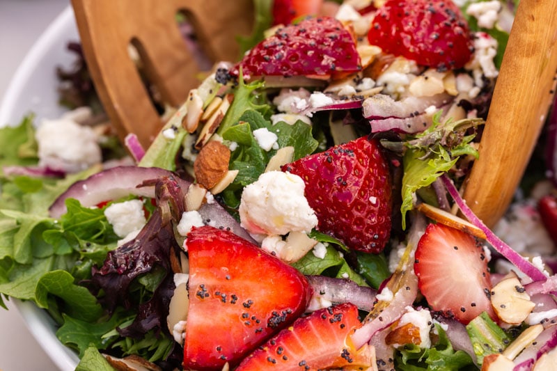 strawberry spinach salad with wooden tongs