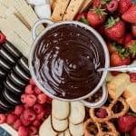 a bowl of chocolate fondue with fruit and cookies on a plate