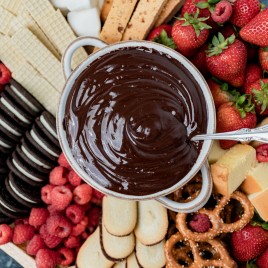 a bowl of chocolate fondue with fruit and cookies on a plate