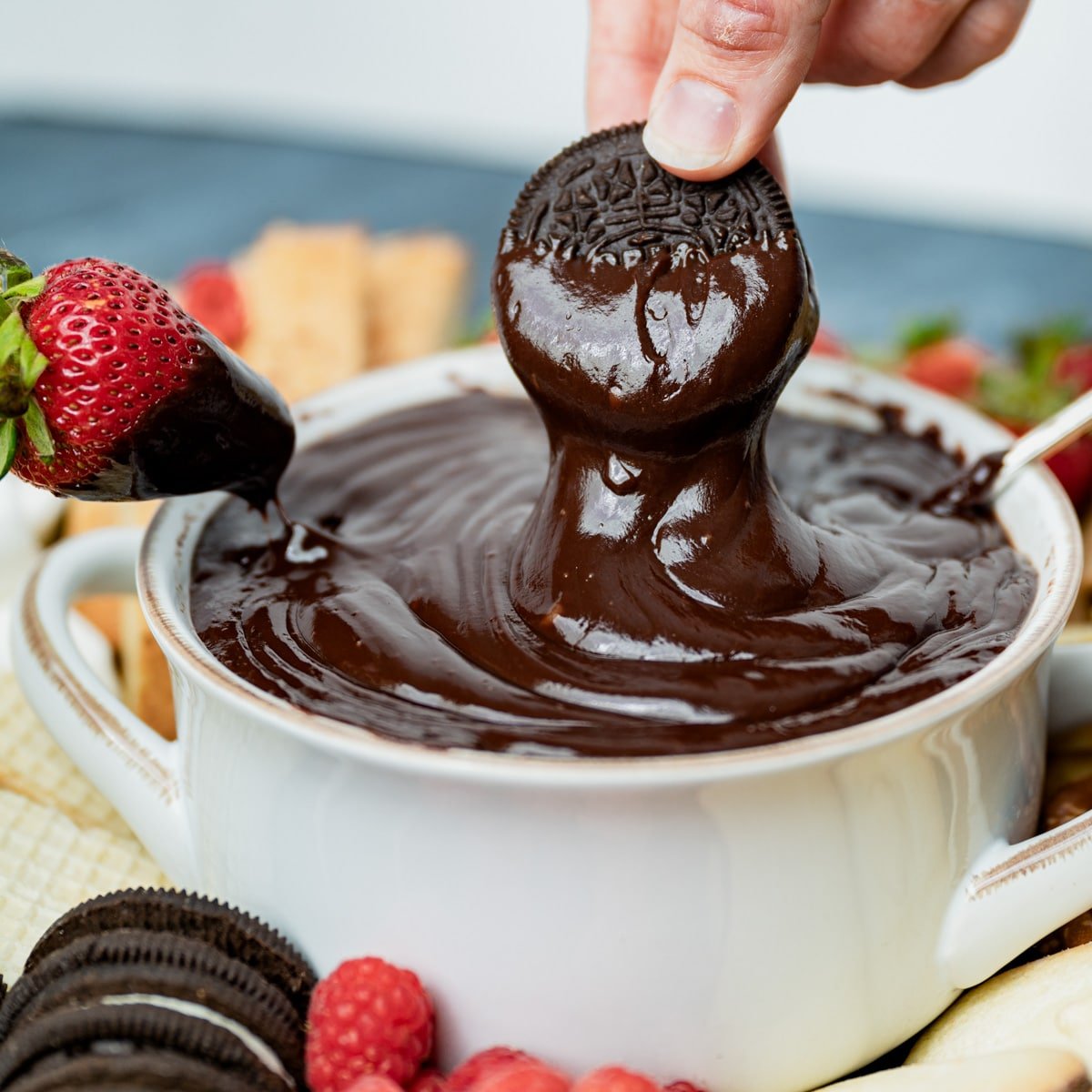 a hand dipping an oreo in chocolate fondue