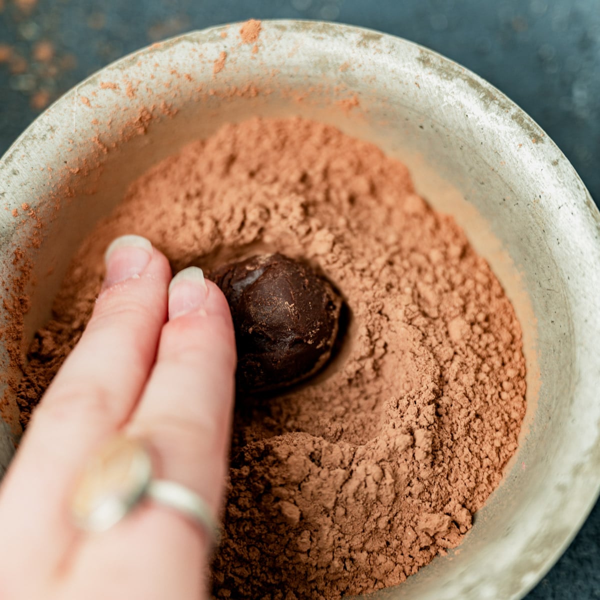 a hand rolling a truffle in cocoa powder