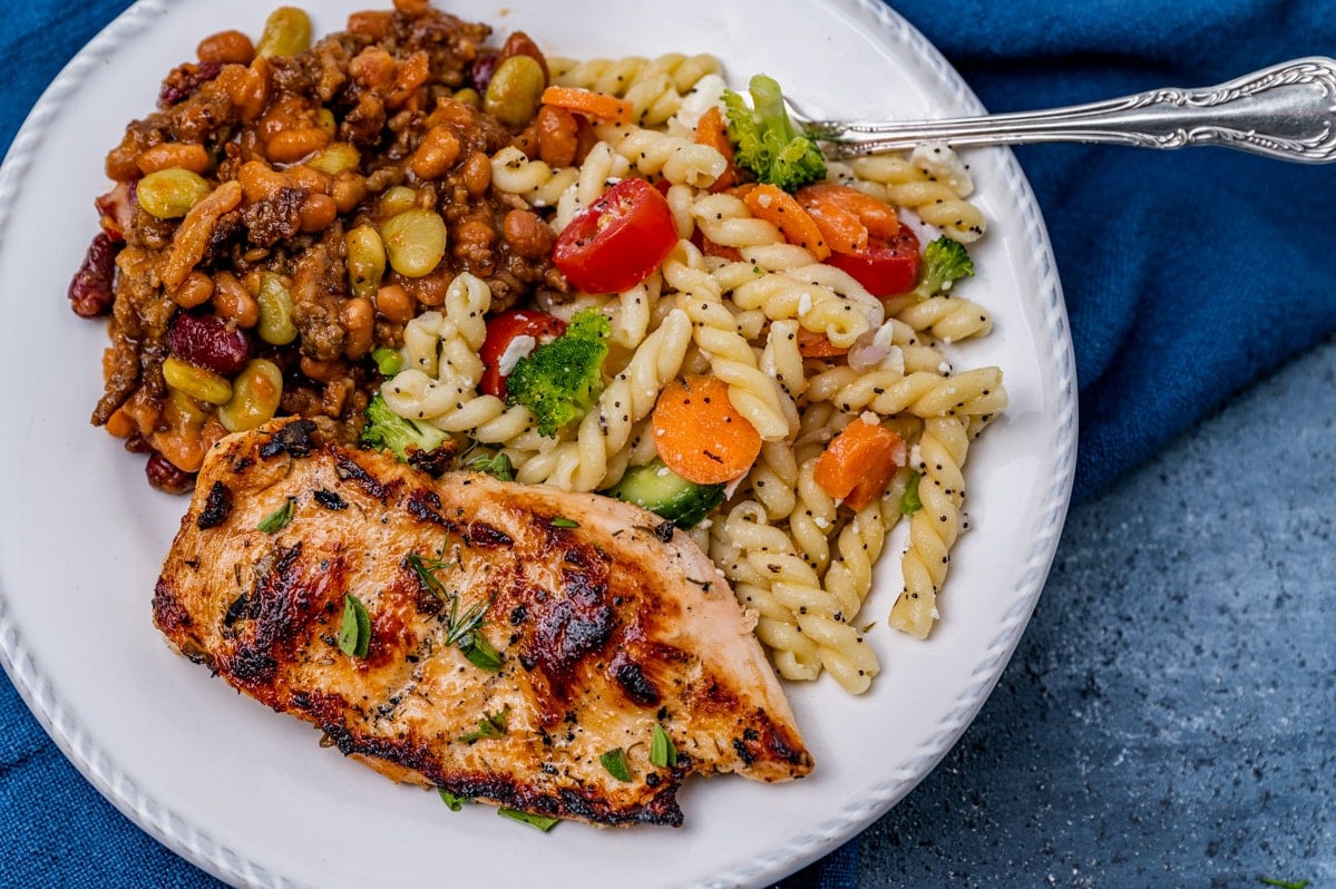 a plate of chicken, pasta salad and beans with a fork