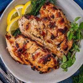 greek chicken in a bowl with fresh herbs and lemons