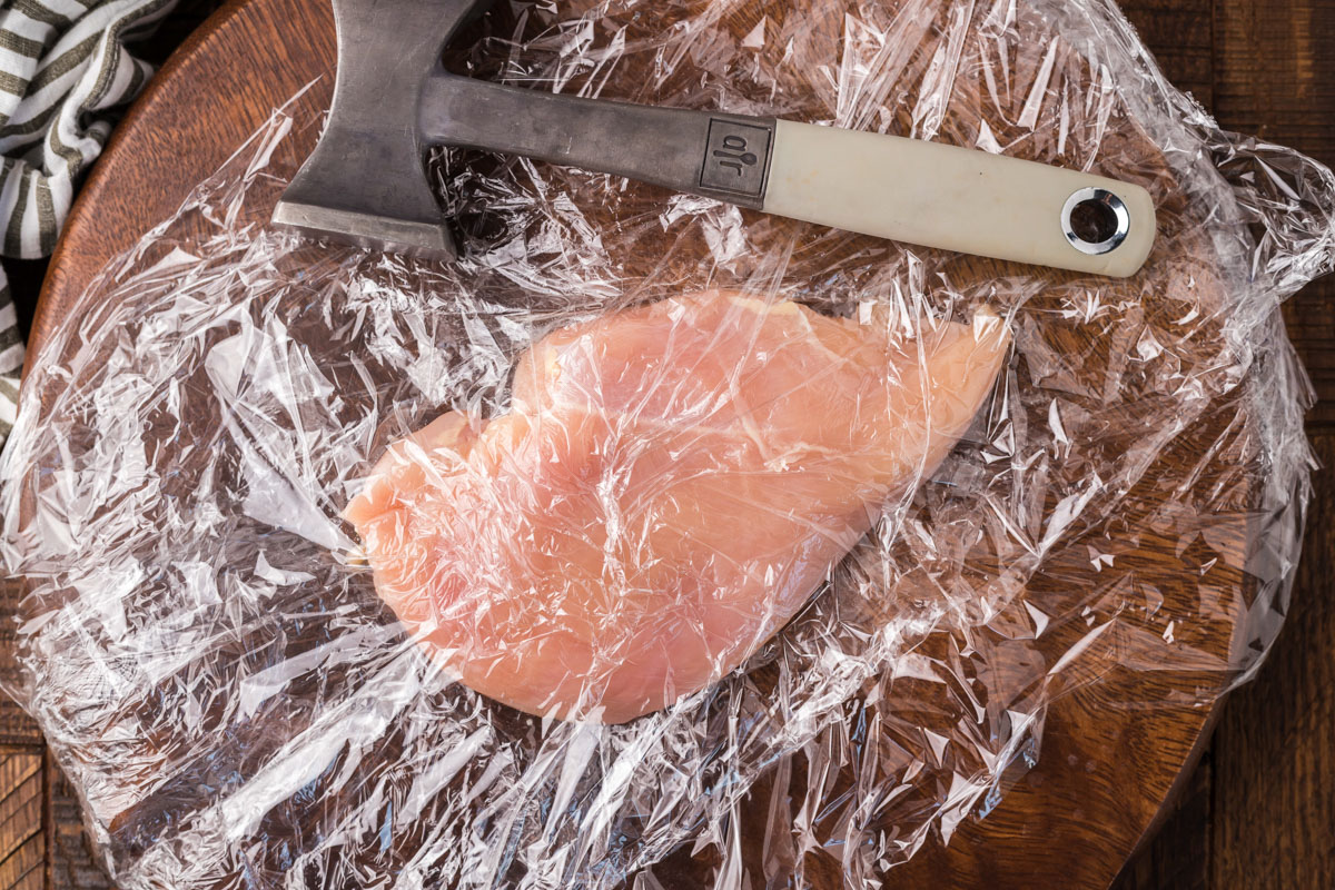 pounding a chicken breast to even thickness in plastic wrap
