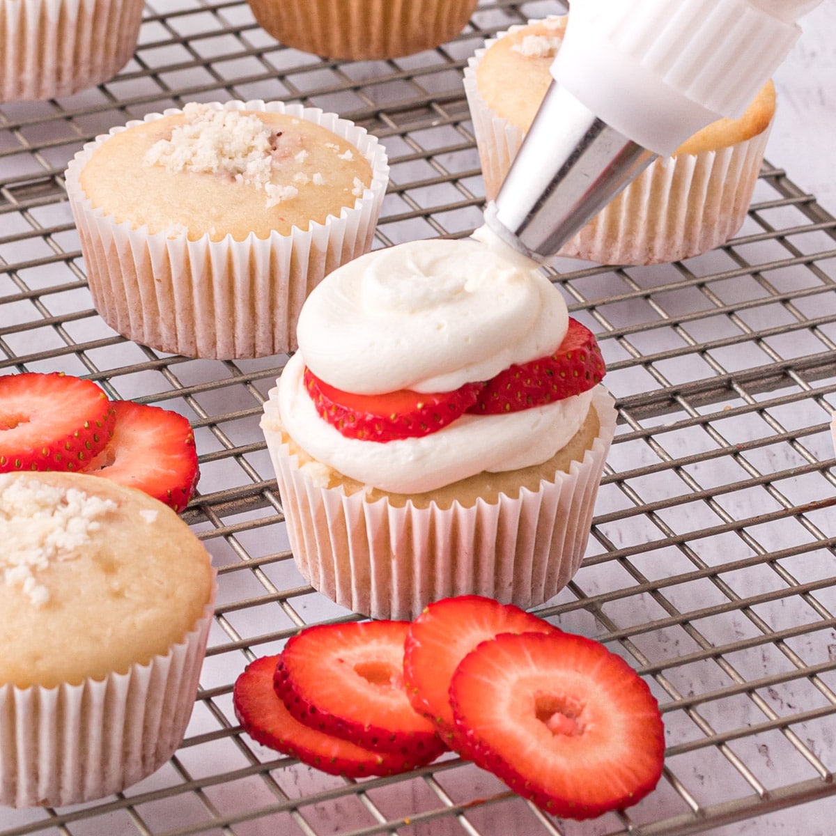 piping whipped frosting on strawberry shortcake cupcakes