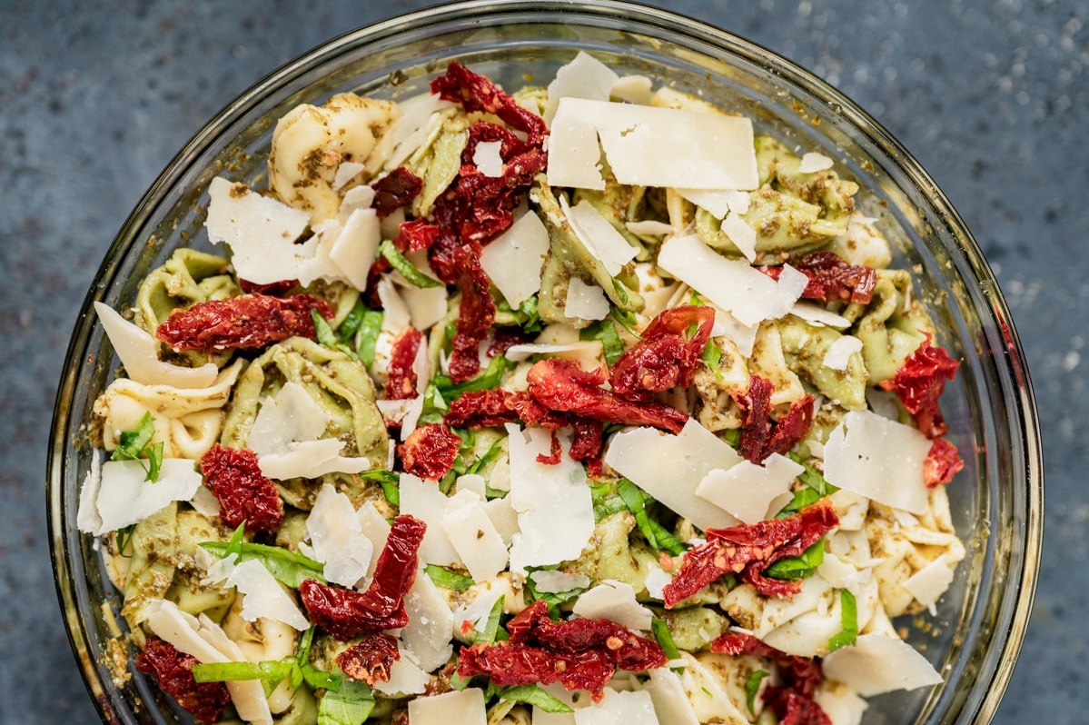 a bowl of pesto tortellini pasta salad with parmesan and sundried tomatoes