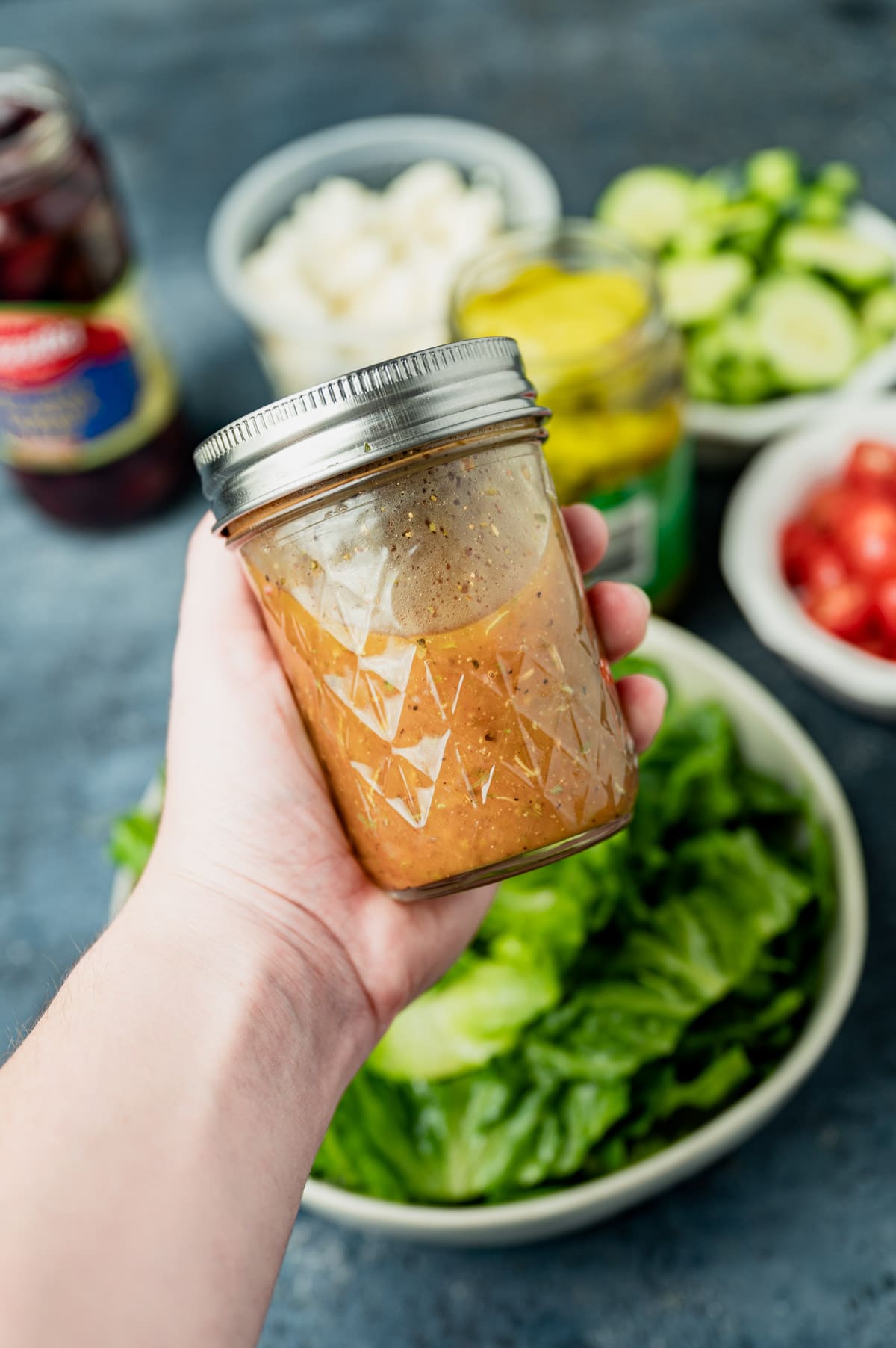 a hand holding a jar of homemade Greek salad dressing