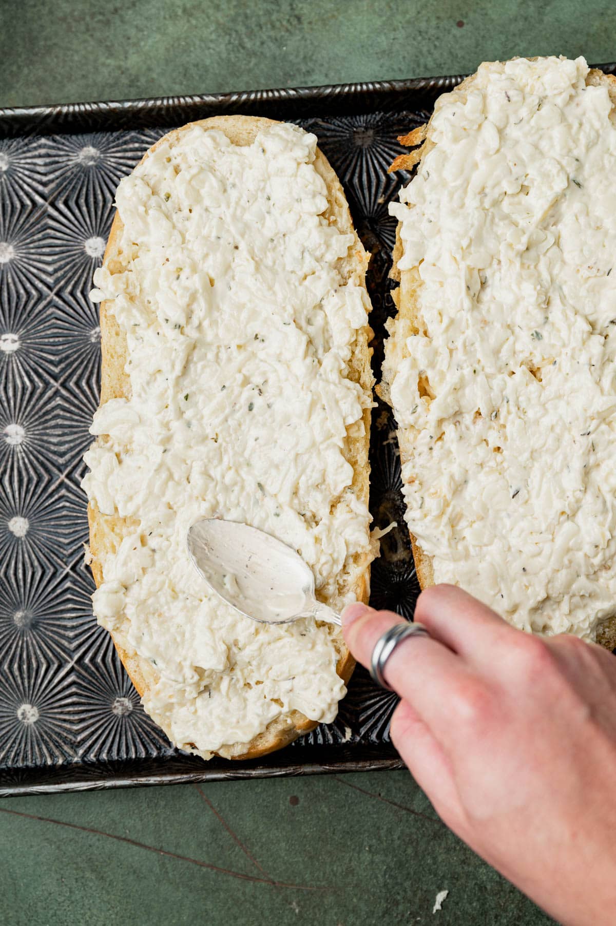 a spoon spreading cheese mixture on a loaf of bread