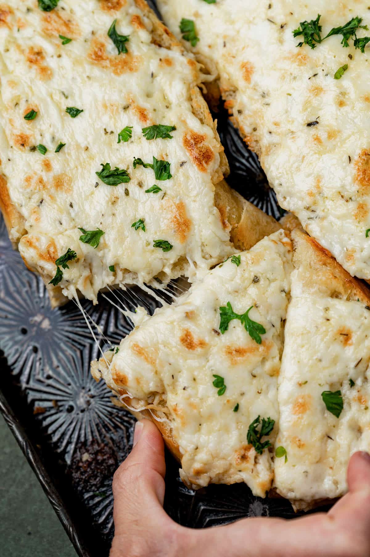 a hand pulling a piece of cheesy garlic bread