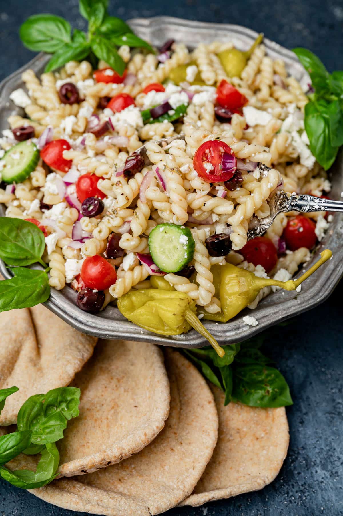 a bowl of greek pasta salad with fresh pitas sitting by it