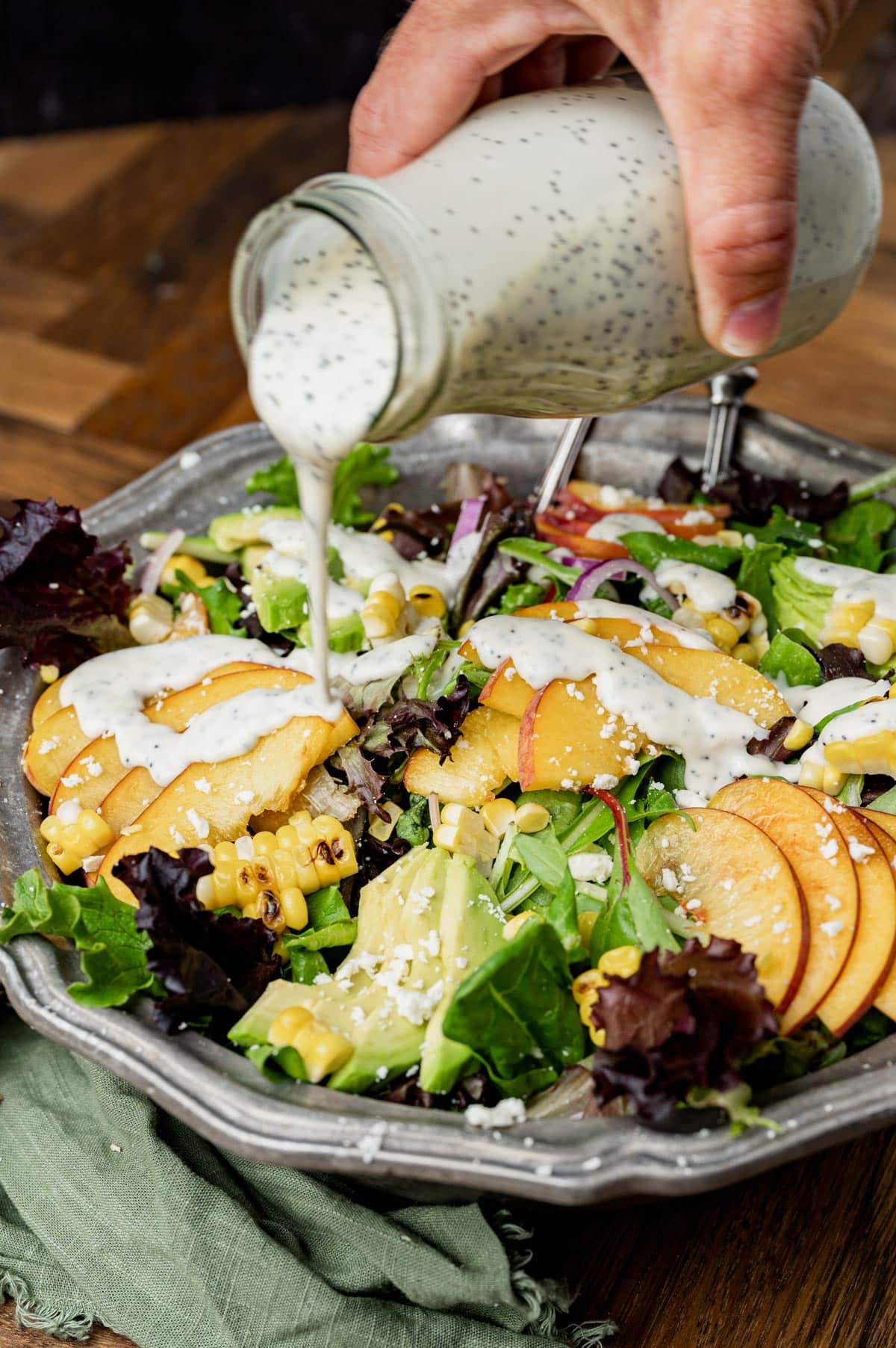 pouring poppy seed dressing over salad in a bowl