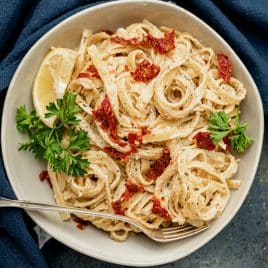 a bowl of sun dried tomato pasta with parsley and a lemon