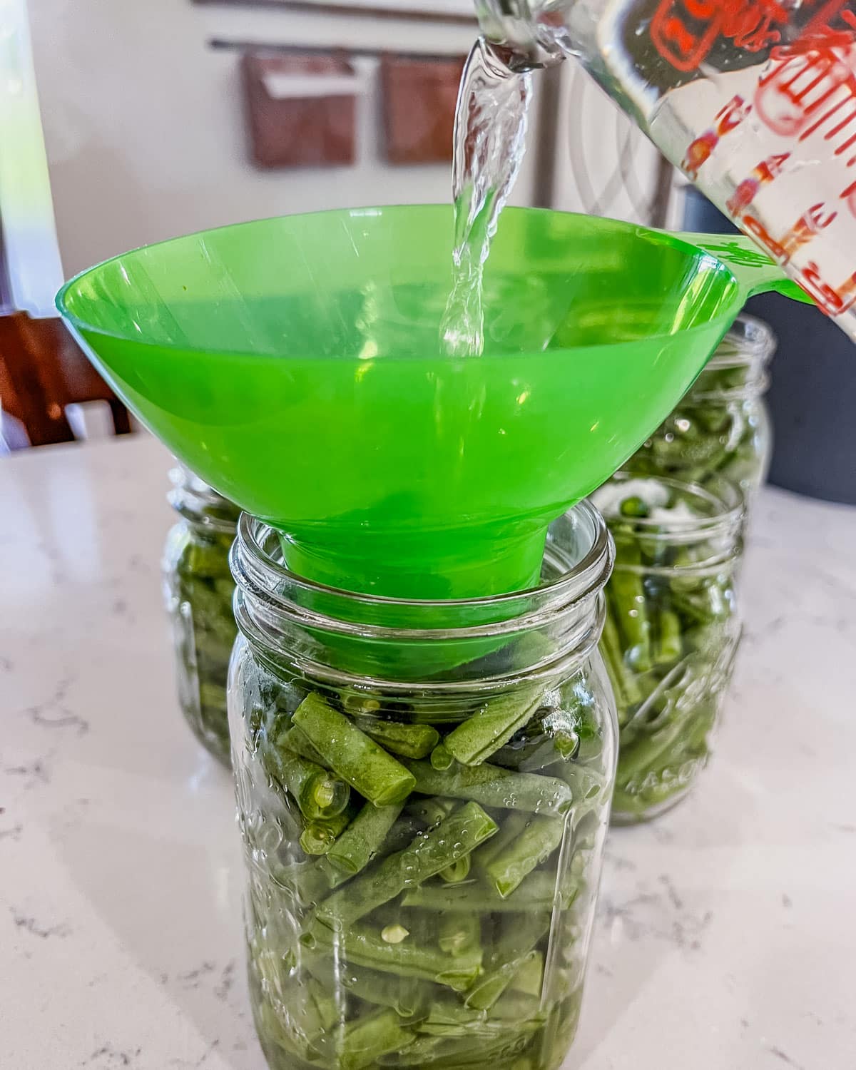 pouring water through a funnel into a jar of green beans