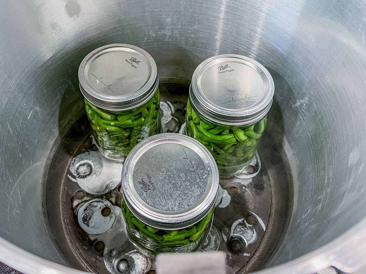 3 quart jars with green beans in a canner