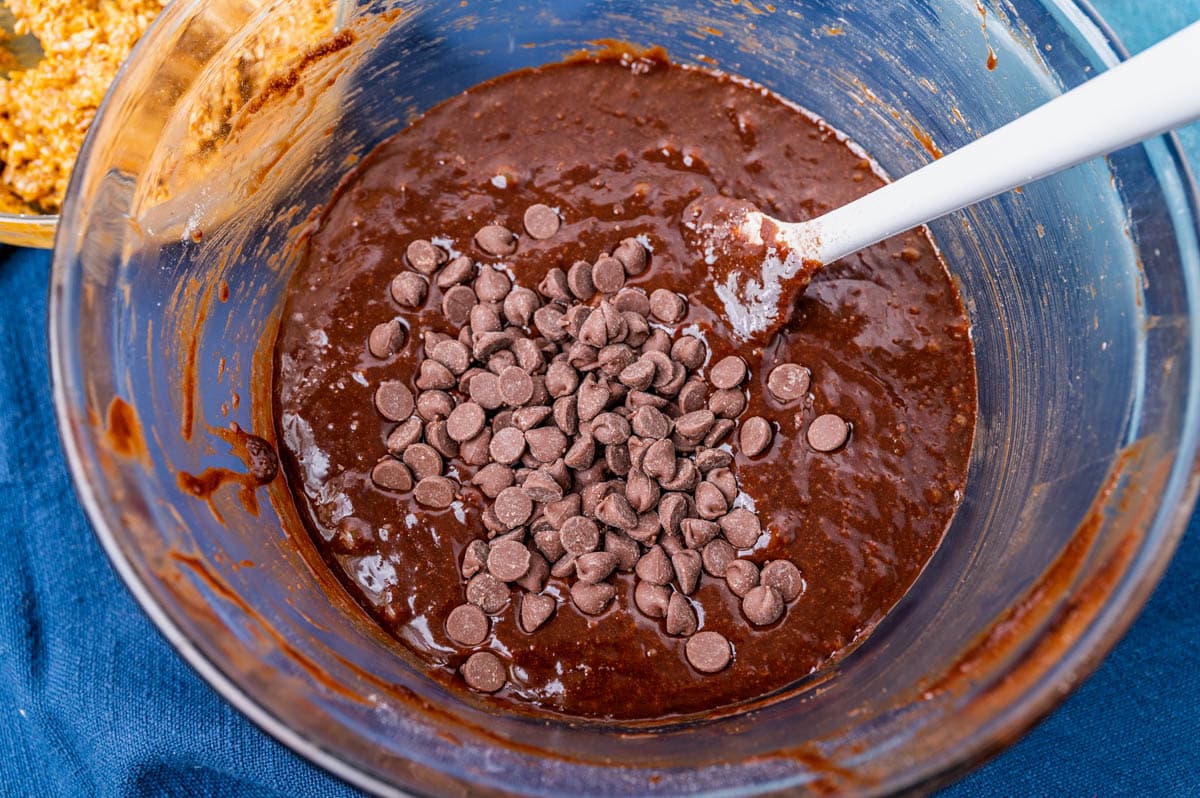 chocolate chips over brownie batter in a bowl