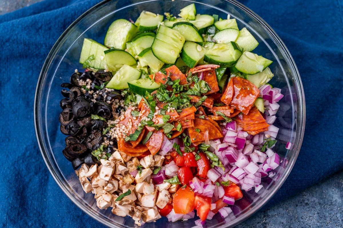 a bowl with olives, mushrooms, tomato, cucumber, pepperoni and vinaigrette in a bowl