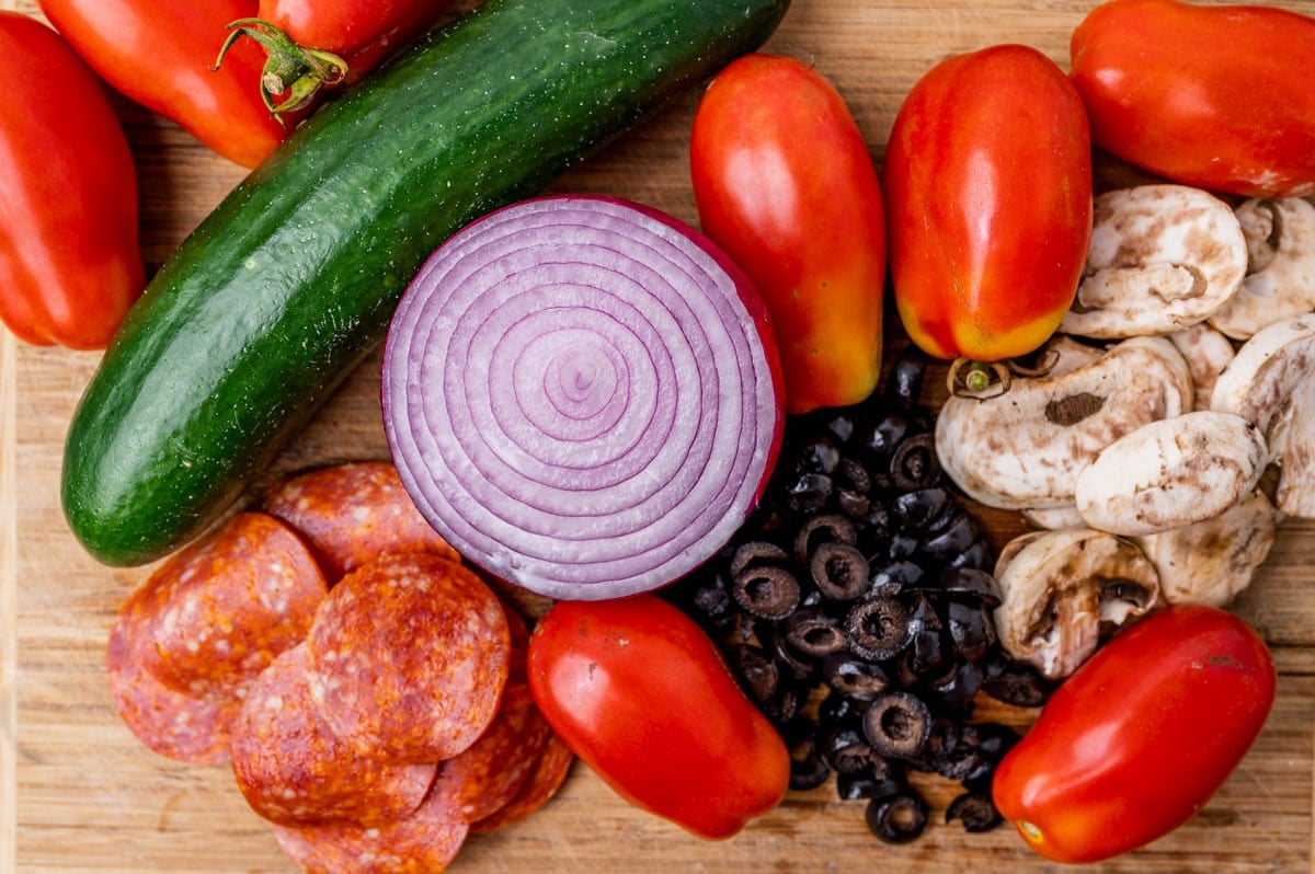 tomatoes, onion, cucumber, olives, mushrooms and pepperoni on a table