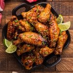 a plate of honey sriracha chicken wings with lime wedges