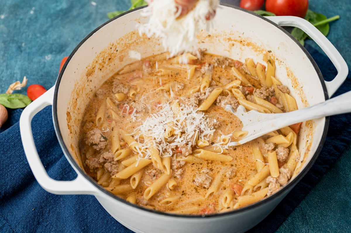 sprinkling shredded parmesan cheese over pasta in a skillet