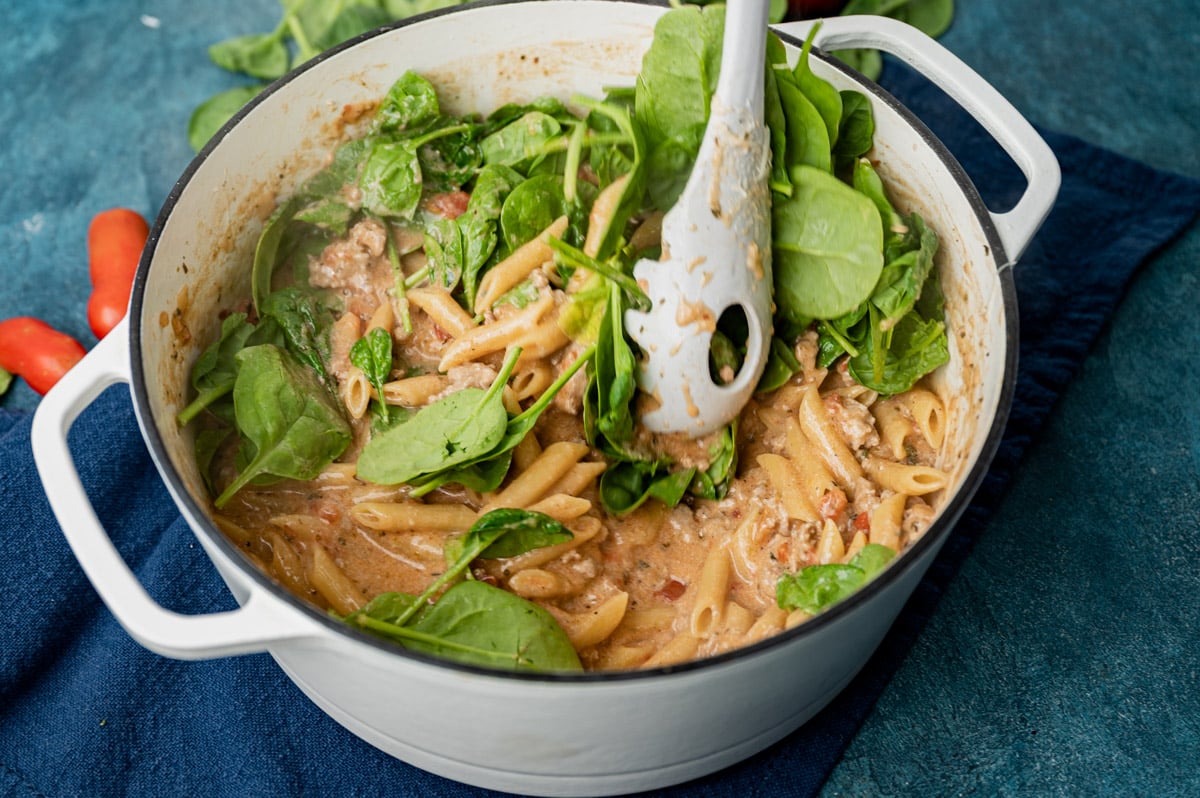 stirring spinach into a ground pork pasta dish