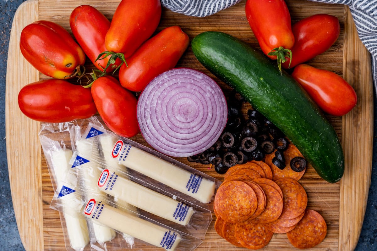 tomatoes, cucumber, cheese sticks, pepperoni, olives and onion on a cutting board