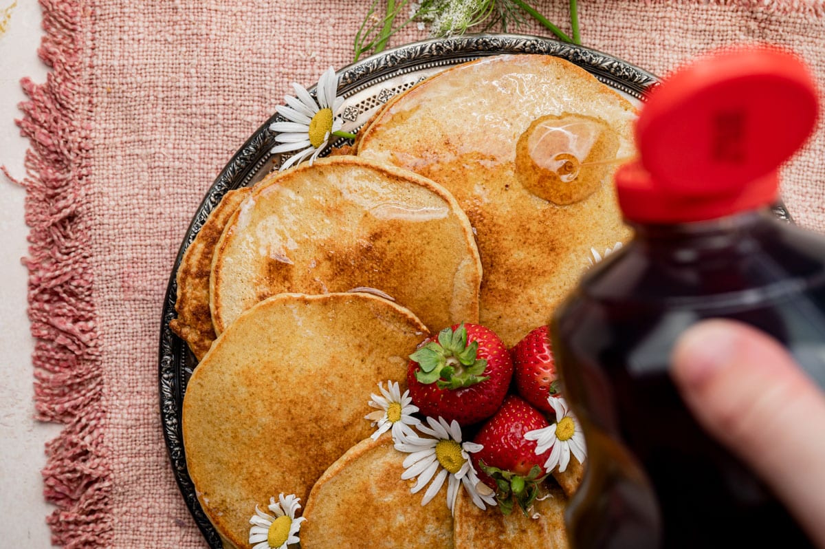 syrup pouring over a plate full of pancakes