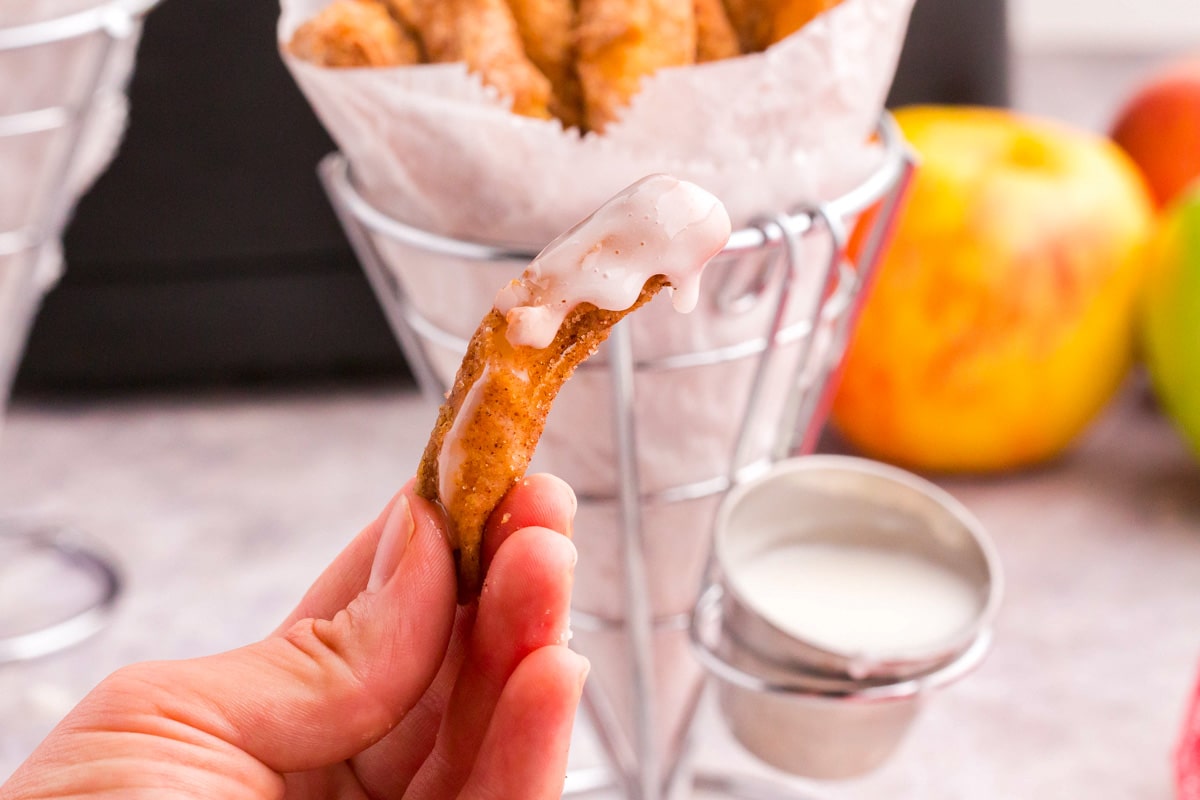 a hand holding an apply fry with vanilla icing