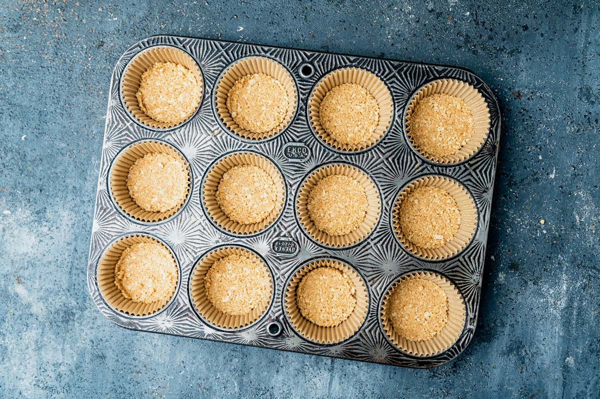 a muffin pan with liners and graham crackers crusts