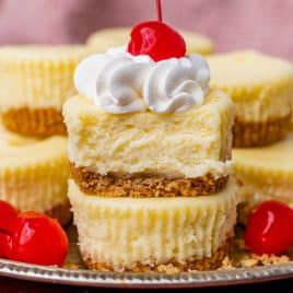 two mini cheesecakes stacked on each other with cherries and whipped cream