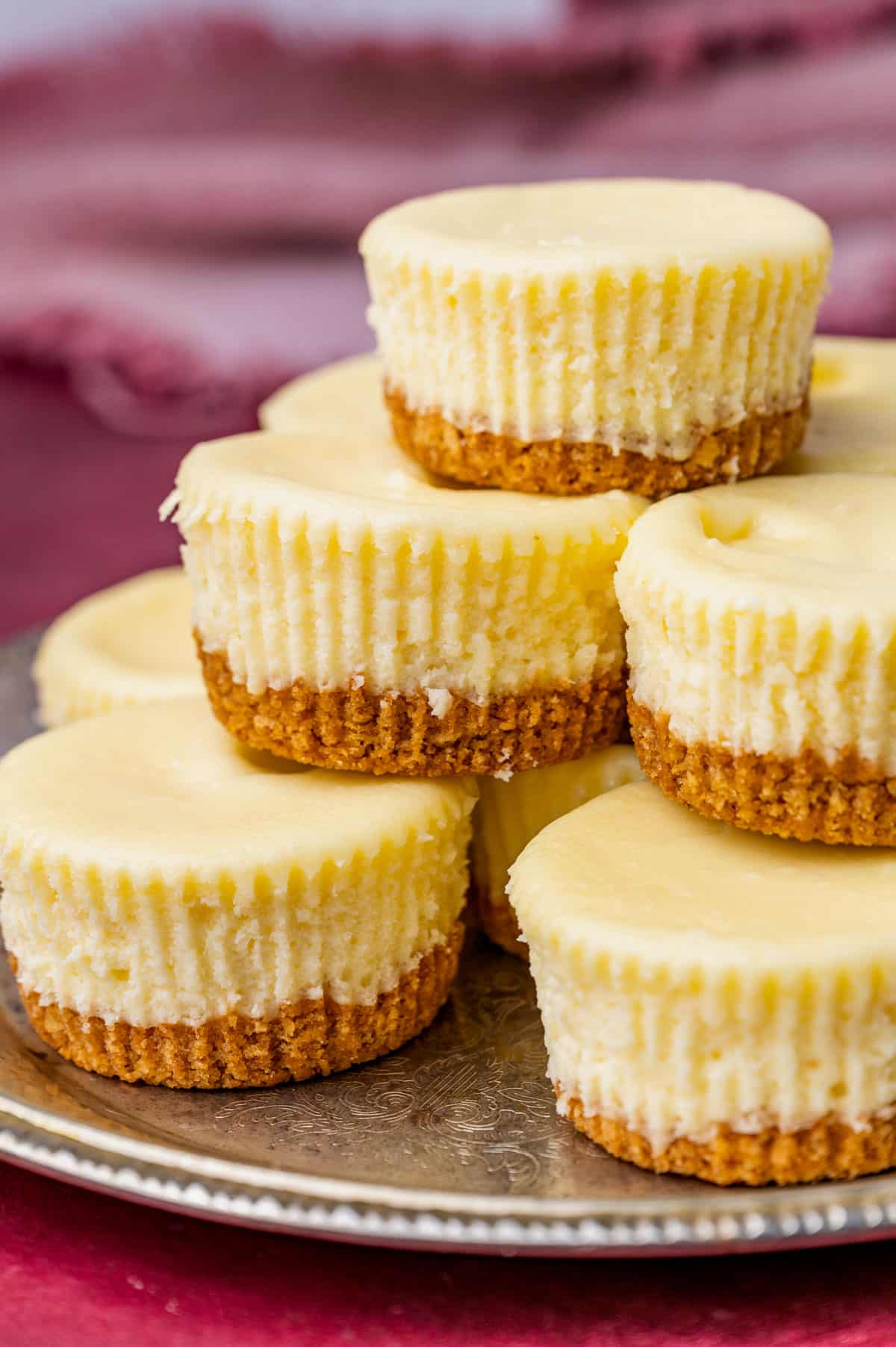 a plate with a pile of plain mini cheesecakes with graham cracker crust