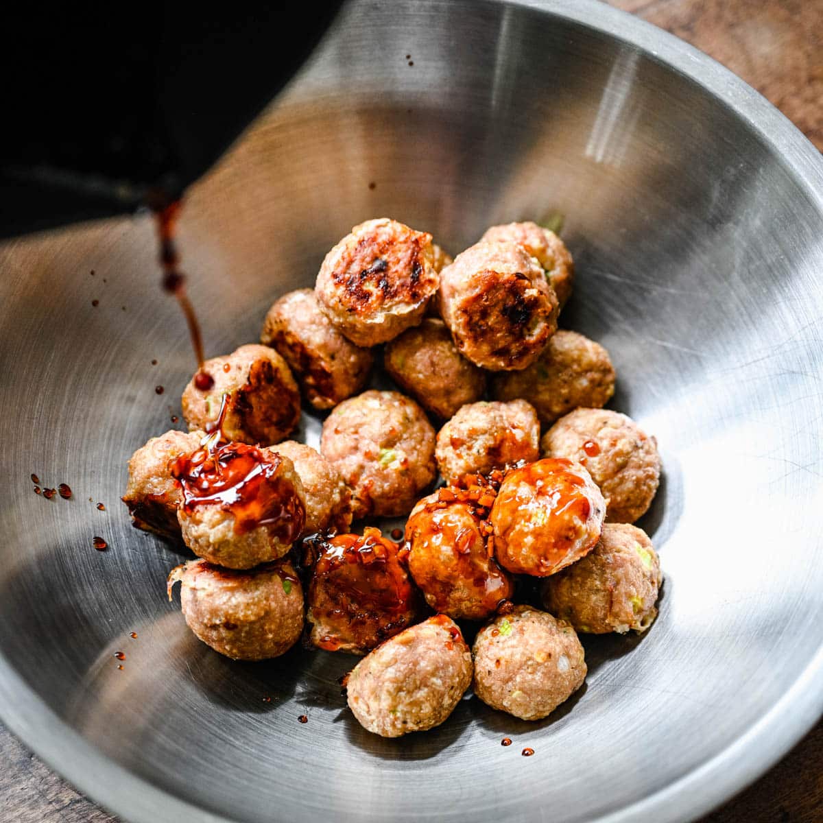 pouring homemade teriyaki sauce over meatballs in a bowl