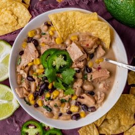 overhead view of a bowl of white chicken chili with tortilla chips and a spoon