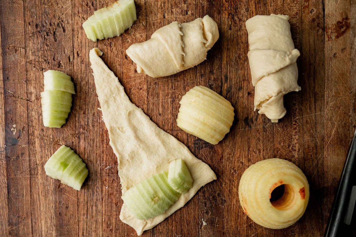 rolling apple slices in a crescent roll on a wooden board