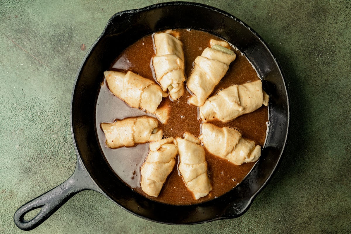 unbaked crescent roll apple dumplings in sauce in a pan