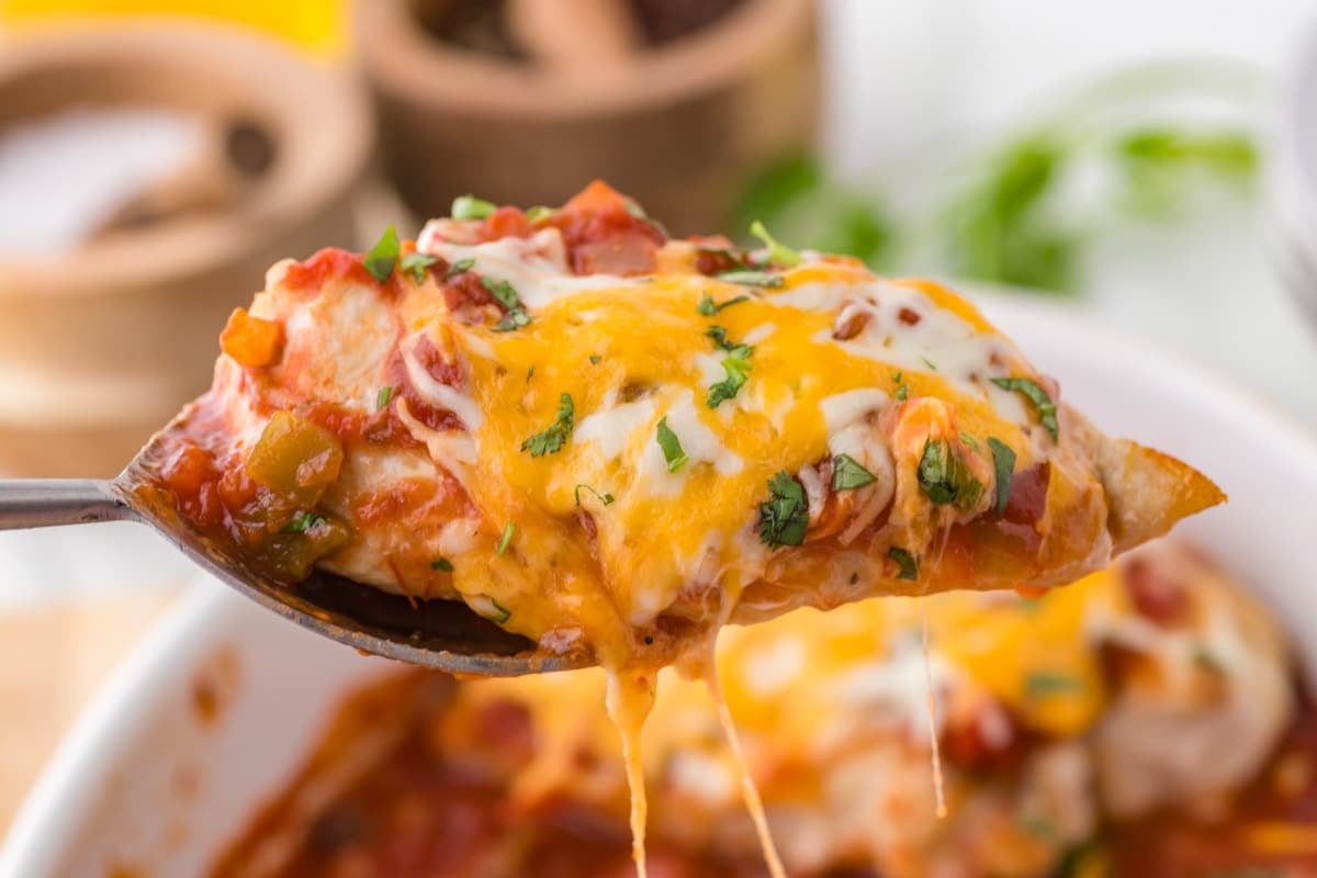a spoon with a baked chicken breast with cheese and salsa on it
