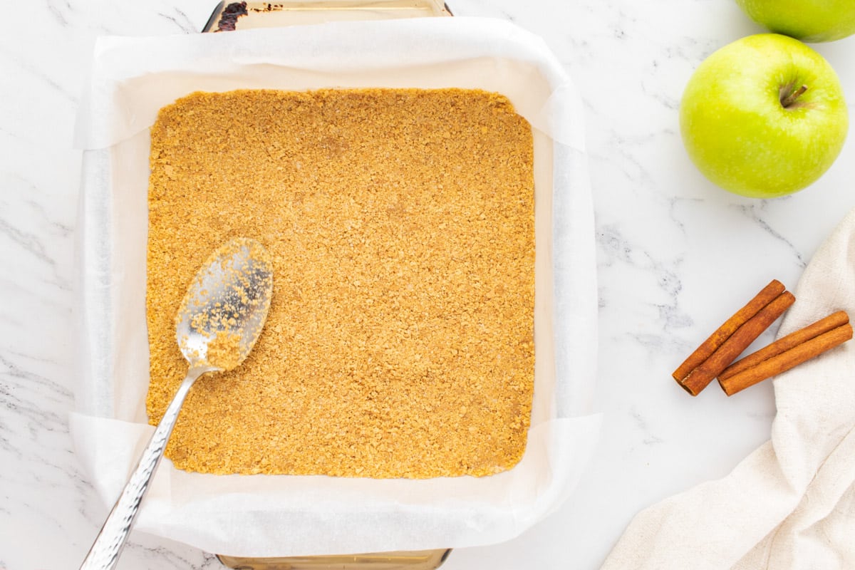 a spoon pressing graham cracker crust in an 8x8 pan